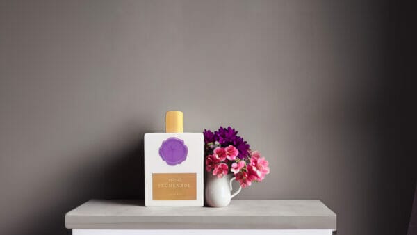 Peitho-Perfumes.ScentedCandles_ A bottle of Prōmenade - Eau de Parfum 100ml sits on a table next to a vase of flowers, emitting its captivating scent.