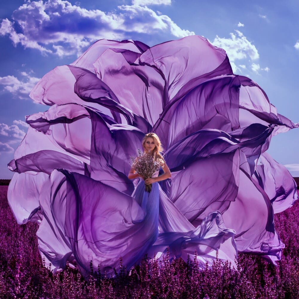 Peitho-Perfumes.ScentedCandles_ A woman in a handmade purple dress standing in a field of lavender, surrounded by the soothing scent of Swiss perfume.
