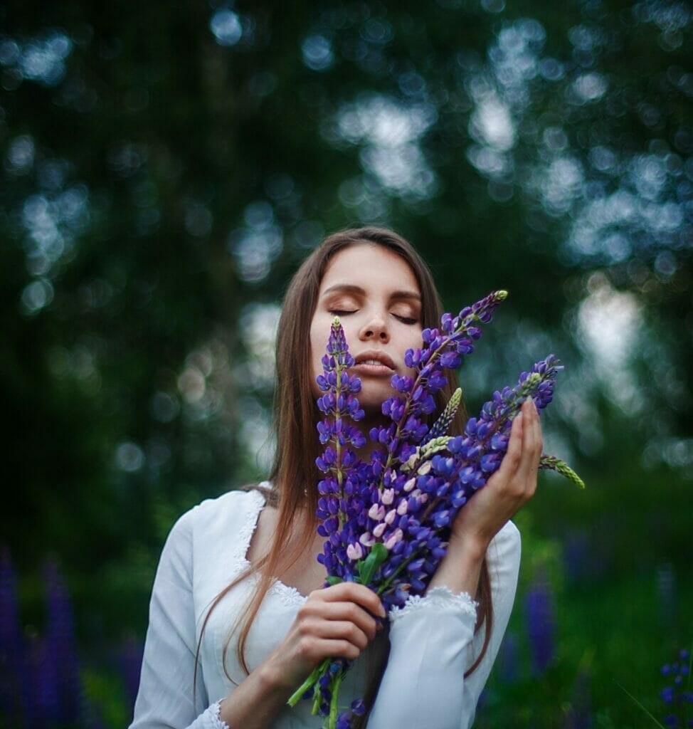 Peitho-Perfumes.ScentedCandles_ A woman is holding a bunch of homemade purple flowers.