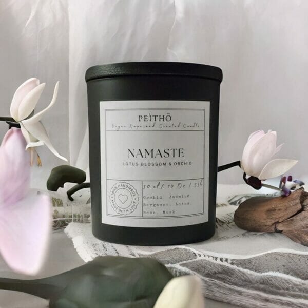 Peitho-Perfumes.ScentedCandles_ black candle jar called namaste next to flowers and wood