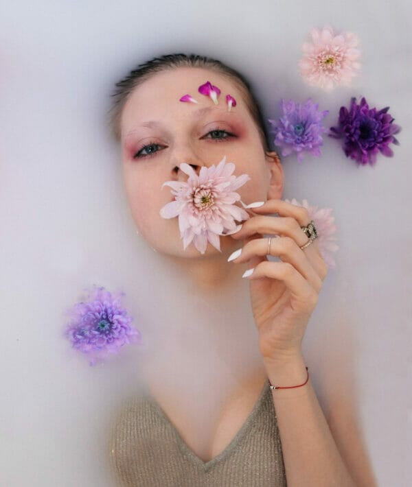 Peitho-Perfumes.ScentedCandles_ A woman in a bath with flowers on her face.