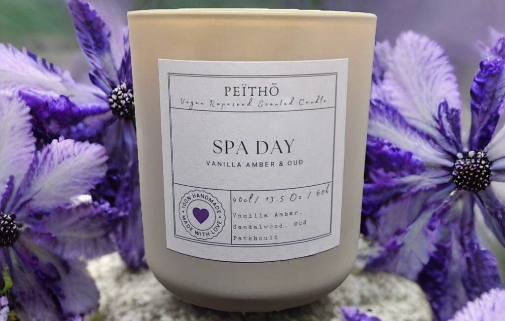 Peitho-Perfumes.ScentedCandles_ A candle with the words spa day sitting on top of purple flowers.